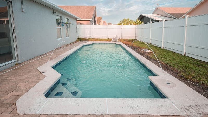 Backyard swimming pool with a white fence and patio area under a partly cloudy sky in Orlando