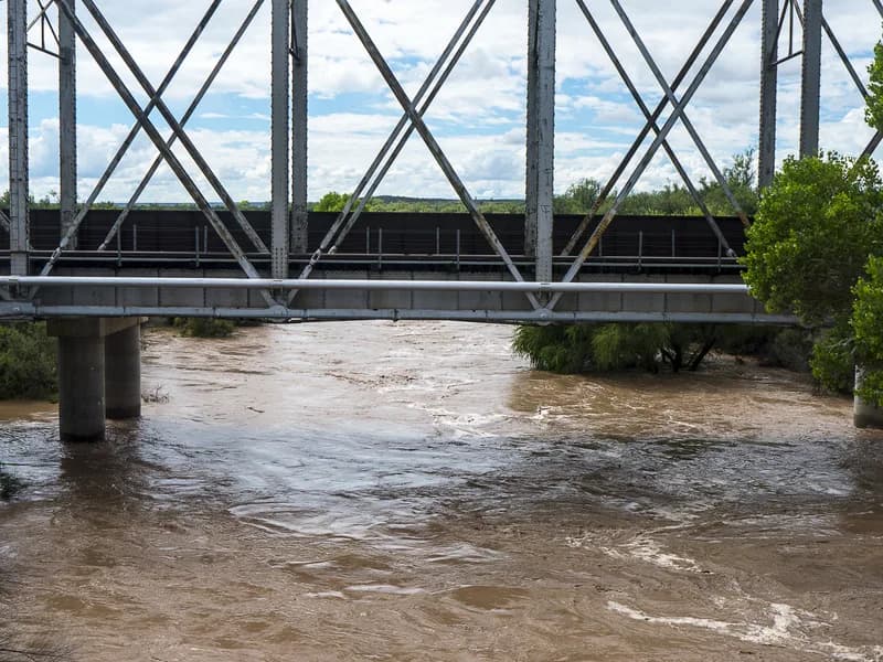 Floodwater pouring over a low earthen dam